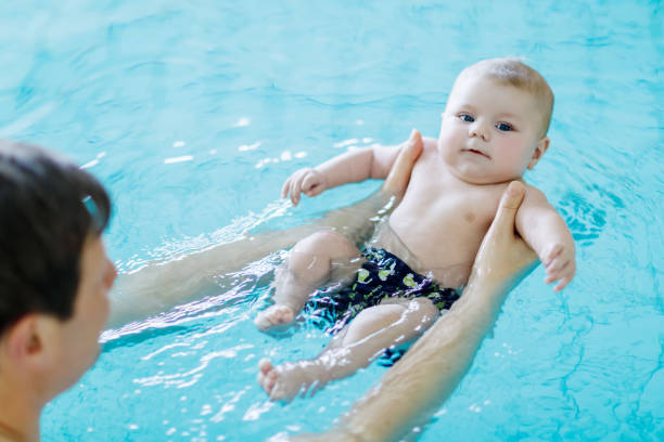 padre de mediana edad feliz nadando con lindo bebé adorable en piscina - bebe bañandose fotografías e imágenes de stock