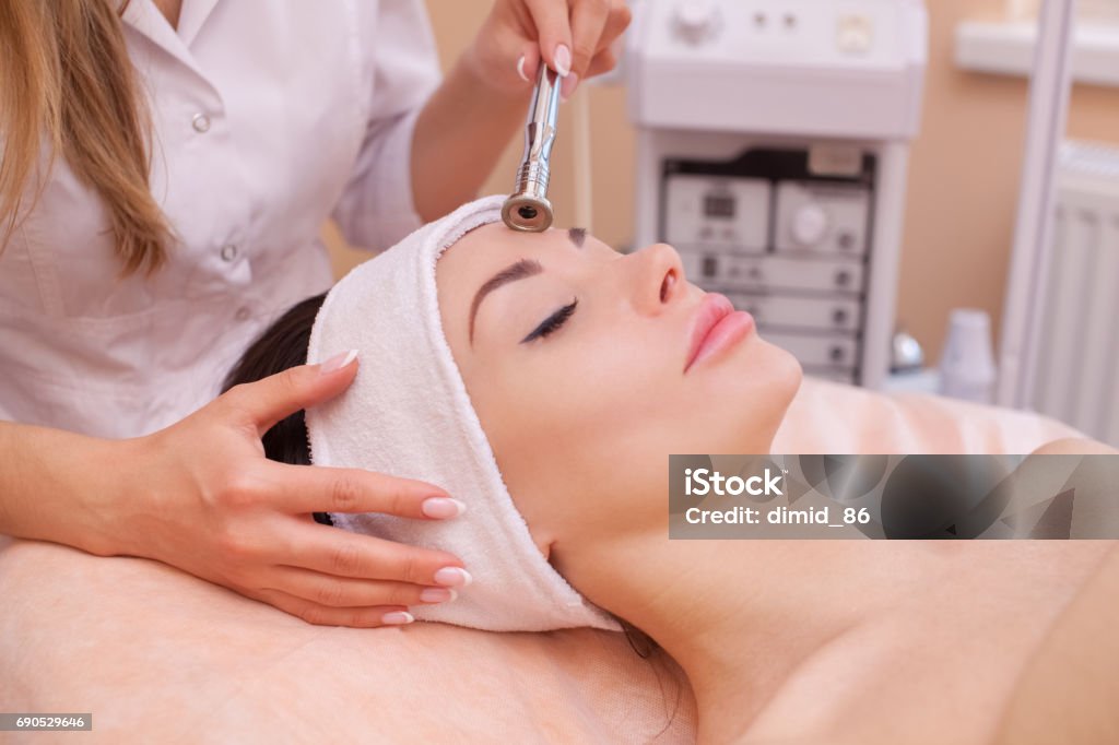 The doctor-cosmetologist makes the procedure Microdermabrasion of the facial skin of a beautiful, young woman The doctor-cosmetologist makes the procedure Microdermabrasion of the facial skin of a beautiful, young woman in a beauty salon.Cosmetology and professional skin care. Human Face Stock Photo