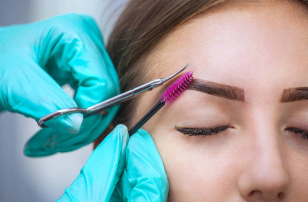 istock Master makeup corrects, gives shape to and cut with scissors previously painted with henna eyebrows in a beauty salon. 690532072