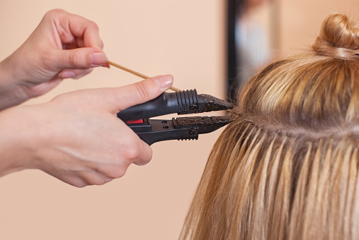 El peluquero hace extensiones de cabello a una joven, una rubia photo