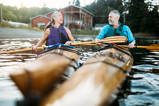 Seniors taking on the world!  A mature couple in their late 50's enjoy paddling their kayaks on a relaxing vacation in Gig Harbor, Washington, the sun shining on the water of the Puget Sound.  A depiction of health and relationship in later years.