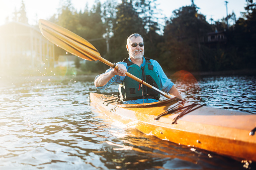Seniors taking on the world!  A mature man is his late 50's enjoys paddling his kayaks on a relaxing vacation in Gig Harbor, Washington, the sun shining on the water of the Puget Sound.