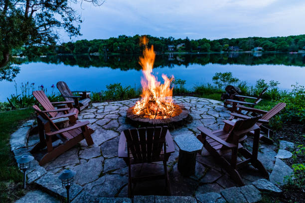 Sitting around the fire Deck chairs around a fire pit on the edge of a lake at dusk fire pit photos stock pictures, royalty-free photos & images