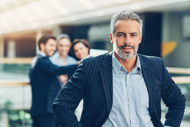 Mid adult businessman with his team behind Mature businessman standing in front of his team group of people men mature adult serious stock pictures, royalty-free photos & images