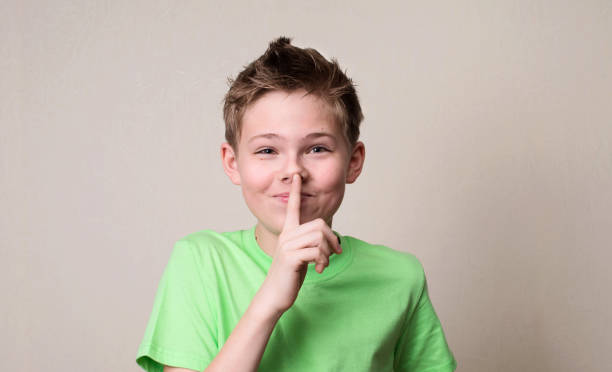 istock Laughing boy doing a silence gesture. Kid putting finger up to lips and ask silence. 690579186