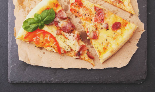 istock Pizza with sausage, ham, tomato and cheese, decorated with basil and cut into pieces 690597560
