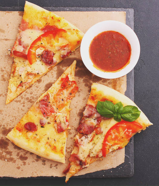 istock Pizza with sausage, ham, tomato and cheese, decorated with basil and cut into pieces 690597946