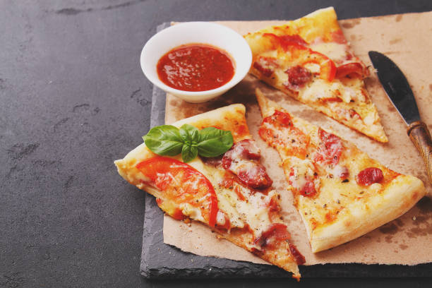 istock Pizza with sausage, ham, tomato and cheese, decorated with basil and cut into pieces 690598322
