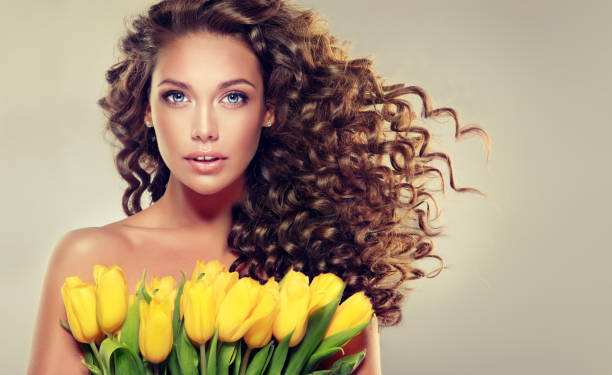若いブルネットの女性は黄色のチューリップを保持しています。 - nature curly hair smiling human face ストックフォトと画像