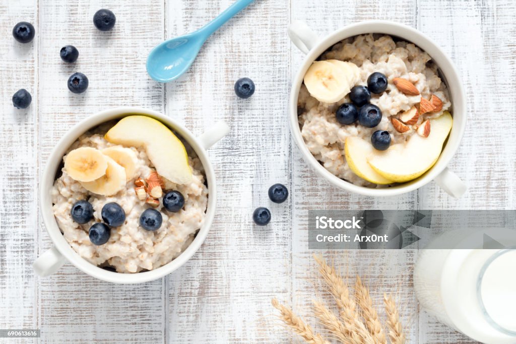 Oatmeal porridge in bowl on white table top view Two bowls of oatmeal porridge with blueberries, pear, banana and almonds on rustic white table background. Table top view Rolled Oats Stock Photo