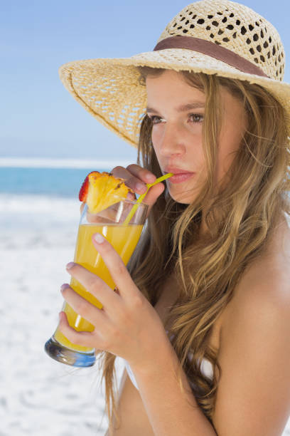 rubia bastante sonriente en bikini bebiendo cóctel en la playa - instructor one person fruit drinking fotografías e imágenes de stock