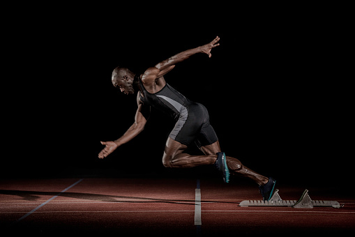 Side view of an African-American sprinter starting to run at the starting blocks.