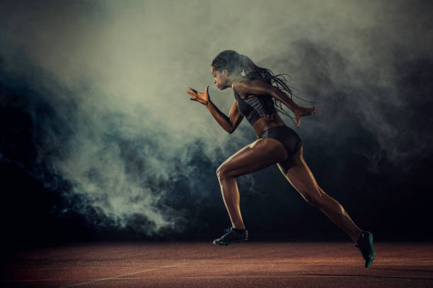 Female runner of African descent in mid-air Side view of a female African-American runner on a red running track. Smoke in the air. track and field athlete stock pictures, royalty-free photos & images