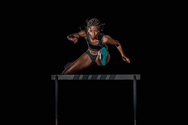 female athlete jumping over a hurdle at night - hurdling hurdle running track event imagens e fotografias de stock