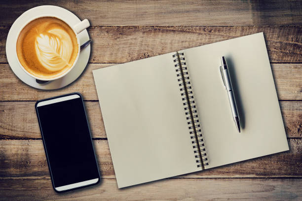 istock Top view notebook, pen, coffee cup, and phone on wood table, Vintage filter. 690667222