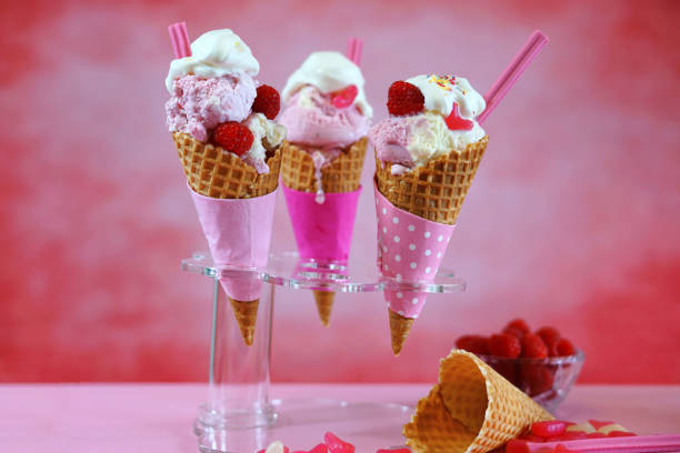 Summertime pink ice cream cones decorated with candy and fruit, meling against a bright pink background.