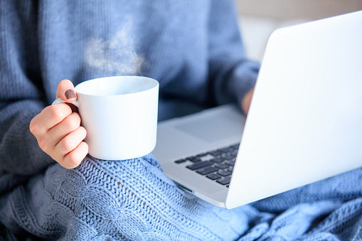 photo of young woman holding cup of coffee and laptop on the wonderful blanket
