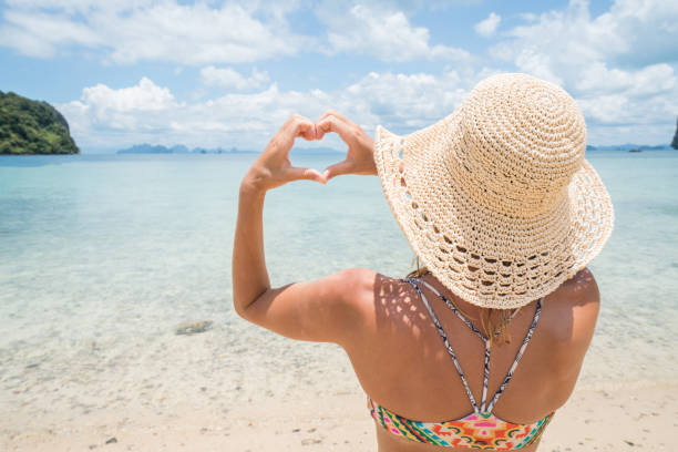 istock Woman making heart shape frame on tropical beach landscape 690681738