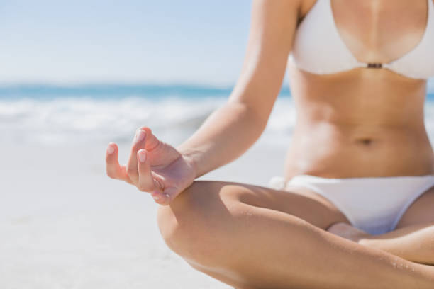 istock Girl in white bikini sitting in lotus pose on beach 690686958