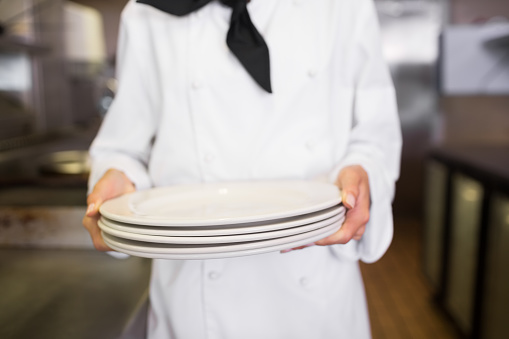 Closeup mid section of a female cook holding empty plates in the kitchen