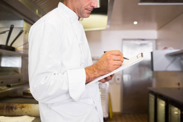 istock Concentrated male cook writing on clipboard in kitchen 690690482