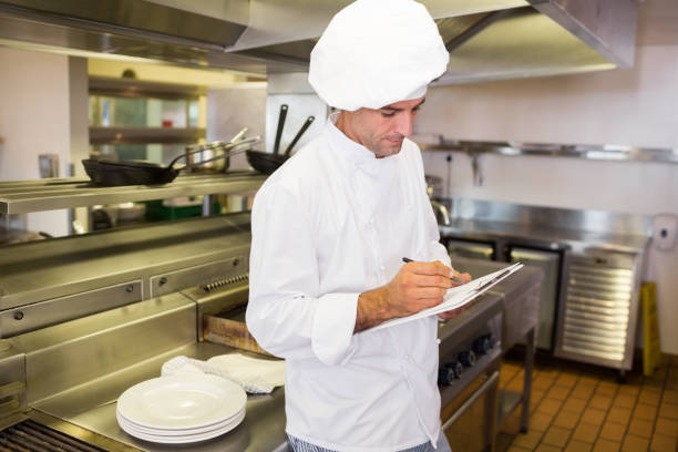 istock Concentrated male cook writing on clipboard in kitchen 690690560