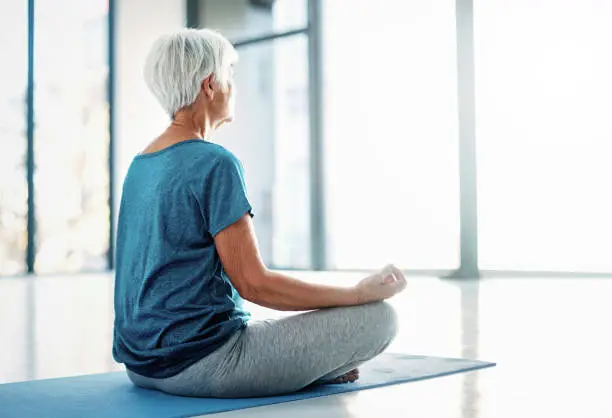 Rearview shot of a senior woman practising yoga indoors