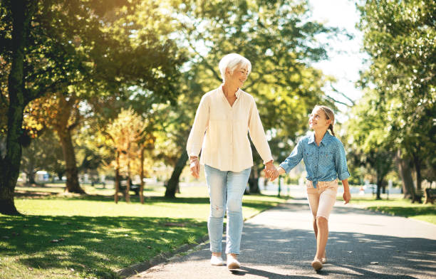 Grandmother walking with her granddaughter. Happy family. Having good times with grandparent outdoors. Golden hour, sunset. Love, connection, bonding. Photo exudes warmth and connection