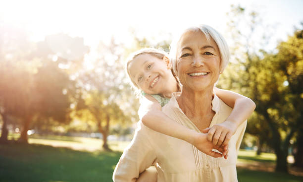 Granddaughters, you gotta love 'em Shot of a little girl and her grandmother enjoying a piggyback ride at the park Grandchild stock pictures, royalty-free photos & images