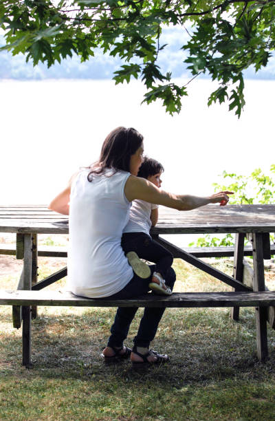 istock Mother with young daughter at picnic table overlooking river. 690720764
