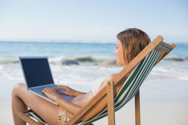 istock Woman relaxing in deck chair on the beach using laptop 690720828