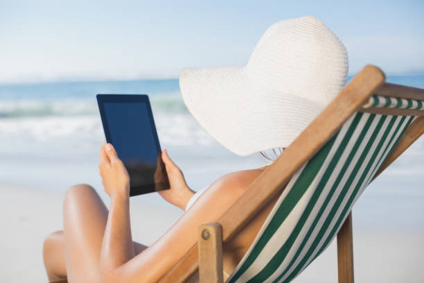 istock Woman relaxing in deck chair on the beach using tablet 690721488