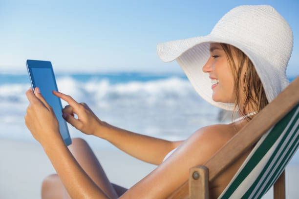 istock Smiling woman relaxing in deck chair on the beach using tablet 690721618