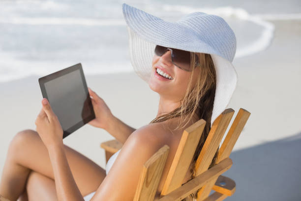 istock Woman in straw hat relaxing in deck chair on the beach using tablet pc 690724124