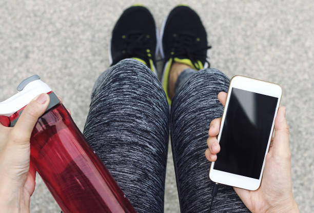 istock Female runner holding smart phone and water bottle while taking break. 690761576
