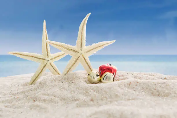 Christmas vacation concept. Two sea stars and christmas bells on the white beach sand with blue sky