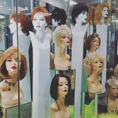 This is a square color photograph shot with a Samsung Galaxy S5 mobile phone in the upper eastside of Manhattan of a window display full of mannequin heads wearing wigs