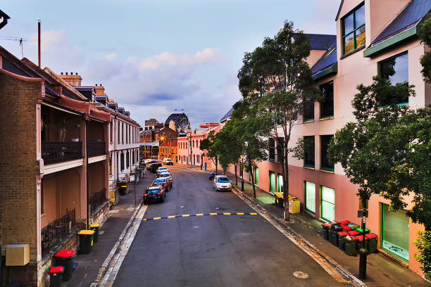 Sydney's eldest suburb The Rocks at sunset from above. Quiet residential street with facades of historic buildings and parked cars towards the Harbour Bridge.
