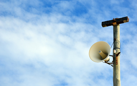 Outdoor loudspeaker warning system on telegraph pole against a blue sky background. Copy space for text.