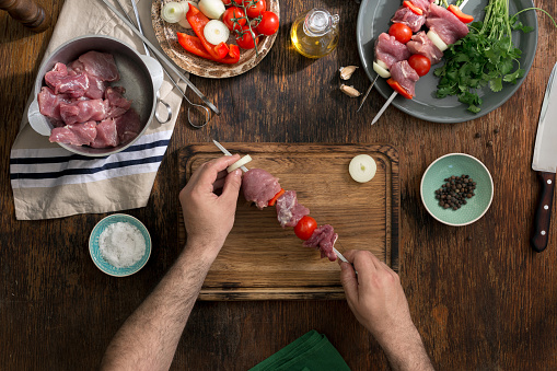 Man cooking shish kebab on a rustic wooden table, top view