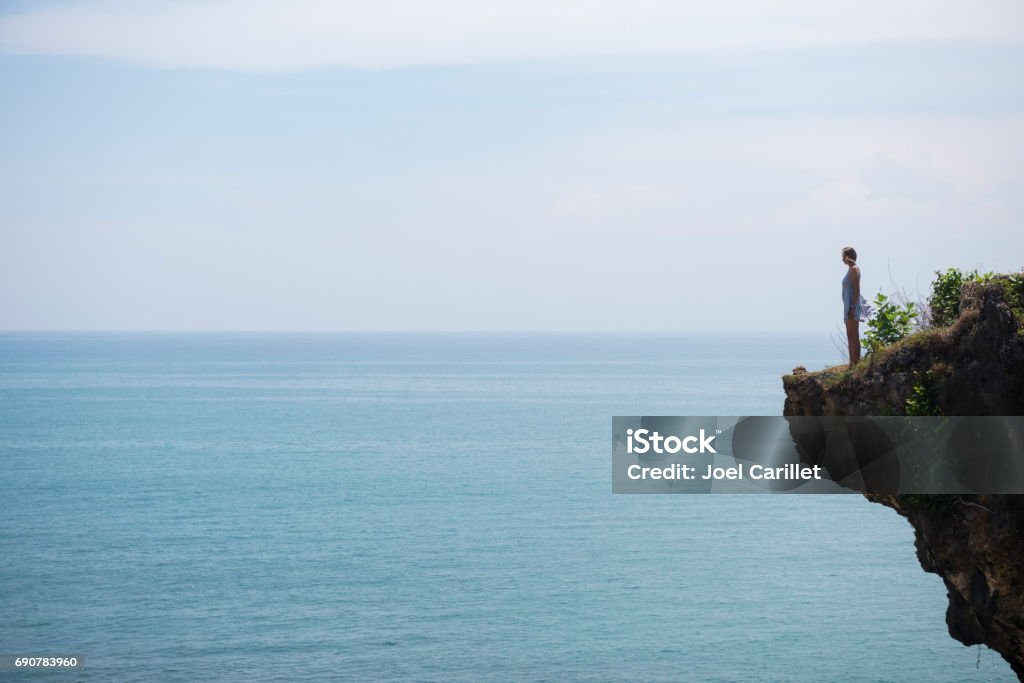 Young woman standing on cliff at Balangan Beach, Bali A young woman visiting Indonesia stands alone on a cliff at Balangan Beach on the island of Bali Above Stock Photo