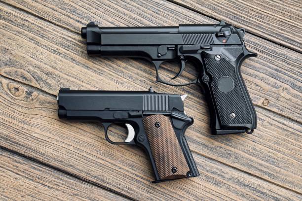 istock Two different hand guns (big and small) on wooden background, .45 pistol small gun. 690787072