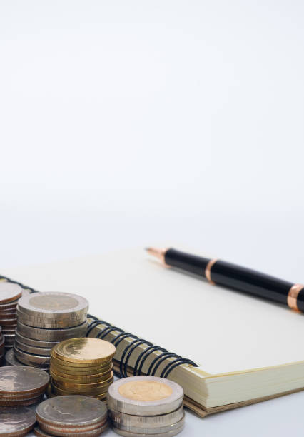 istock vertical close up Thai coins stack in a row with ball pen and note book on white desk for saving; finance; investment; banking concept. 690800182