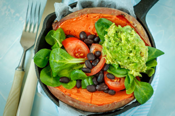 Baked whole sweet potato with guacamole and black beans in a cast-iron frying pan.