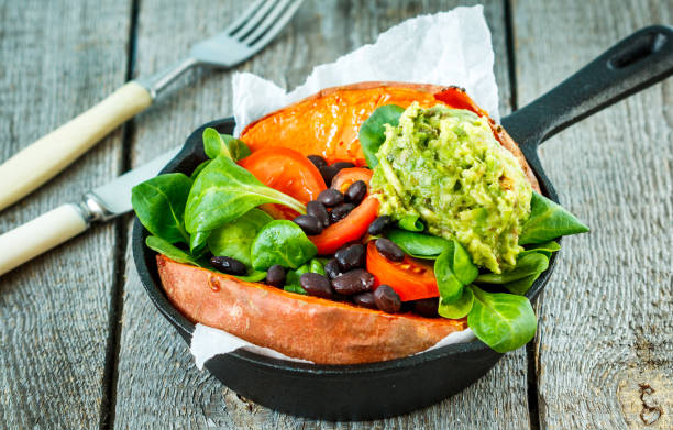 Baked whole sweet potato with guacamole and black beans in a cast-iron frying pan.