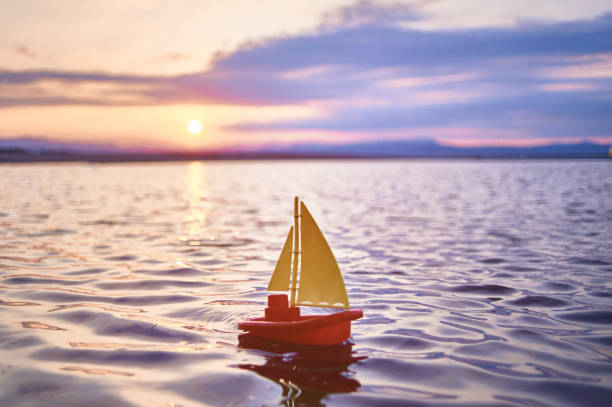 A small children's yellow red boat sails on the sea against the background of the sunrise A small children's yellow red boat sails on the sea against the background of the sunrise. yellow nail polish stock pictures, royalty-free photos & images