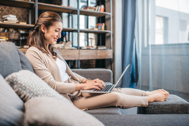 istock smiling woman working on laptop while relaxing on sofa 690837730