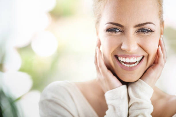 Serenity. Closeup portrait of an attractive mid 30's woman gently touching her neck and smiling while looking at the camera and sincerely smiling. Blurry green background. Toothy Smile stock pictures, royalty-free photos & images