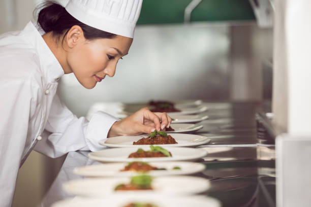 chef donna concentrata guarnire il cibo in cucina - hat women chef occupation foto e immagini stock