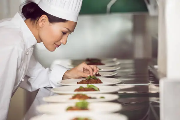 Photo of Concentrated female chef garnishing food in kitchen